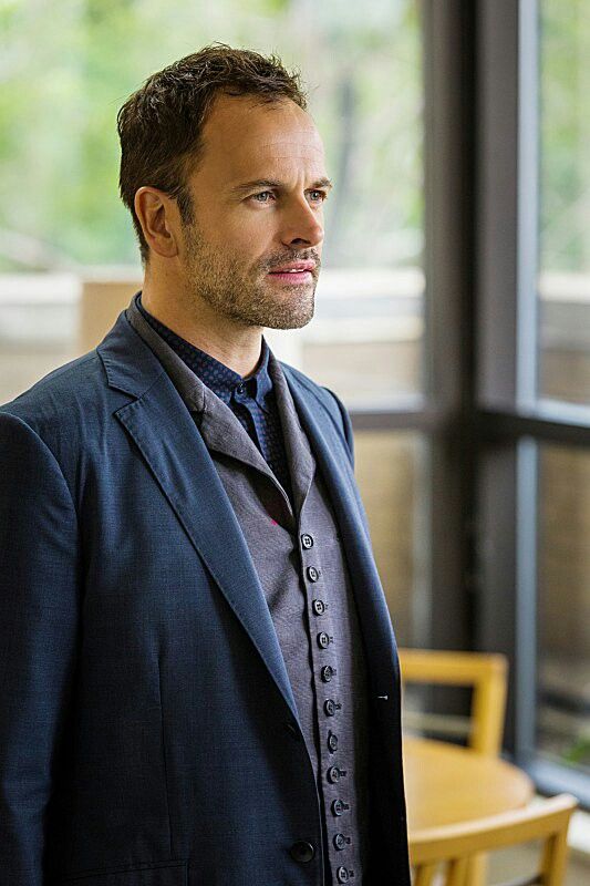 a man in a suit and tie standing next to a window looking off into the distance