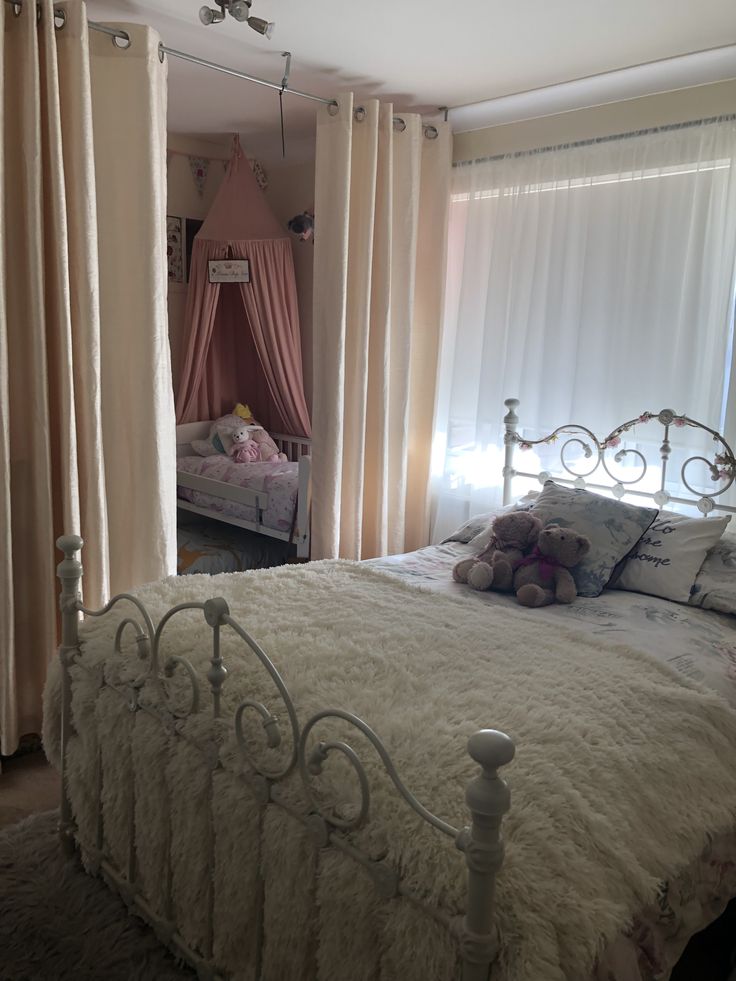 a white bed sitting in a bedroom next to a window with pink drapes on it