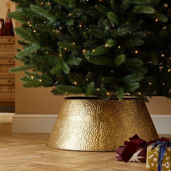 a small christmas tree in a gold pot with presents under it and the lights on