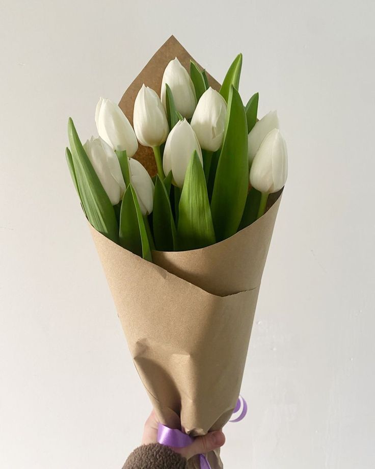 a person holding a bouquet of white tulips in their hand with a brown paper wrapped around it