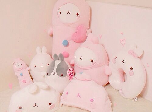 a group of stuffed animals sitting next to each other on a white surface in front of a pink wall