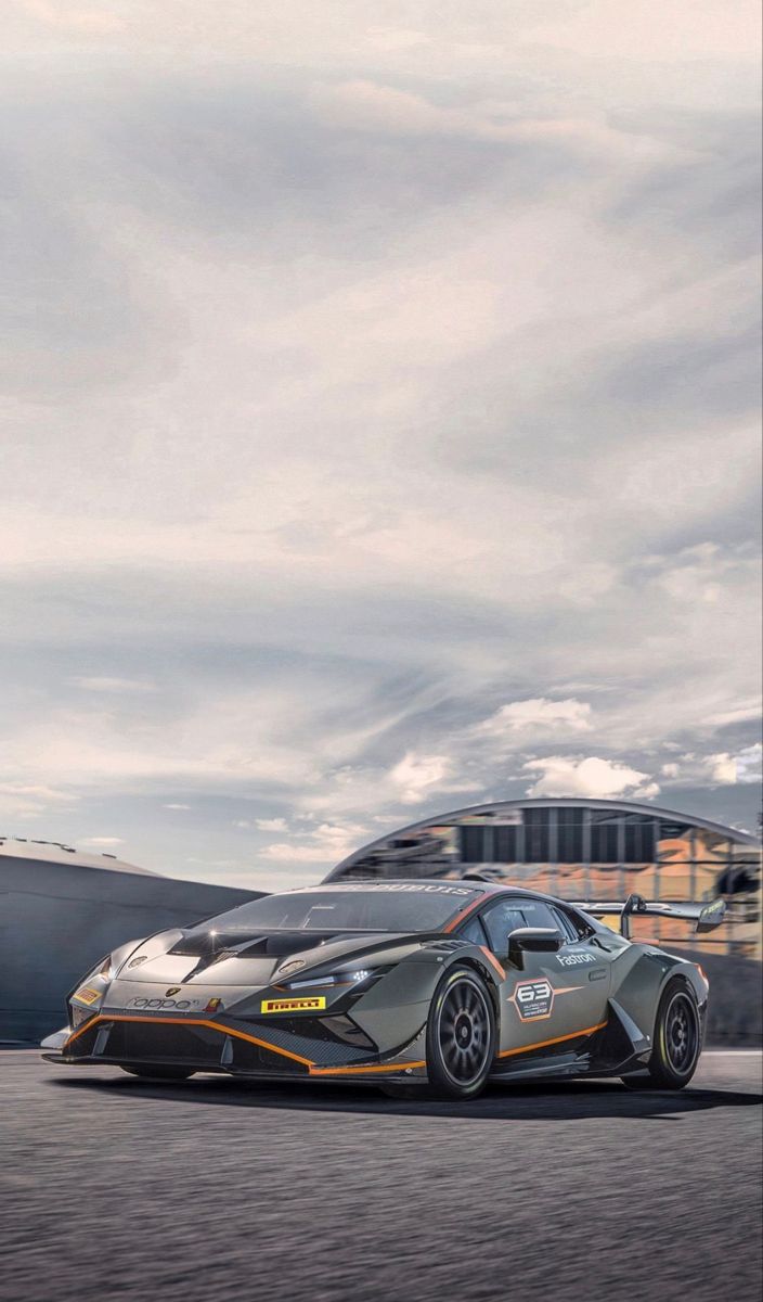 a silver and orange sports car driving down the road next to a large boat in the background