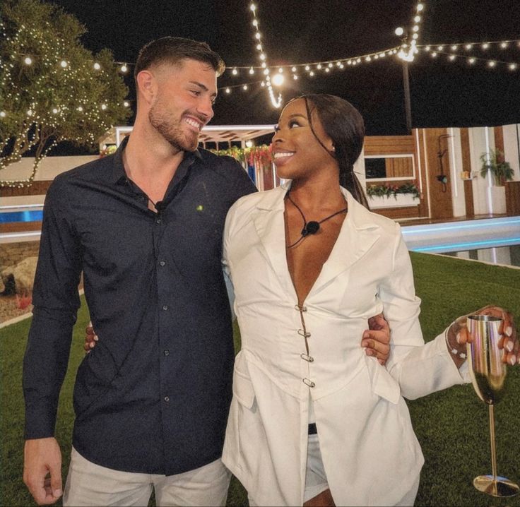 a man and woman standing next to each other in front of a pool at night