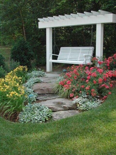 a white bench sitting in the middle of a garden next to flowers and plants with rocks