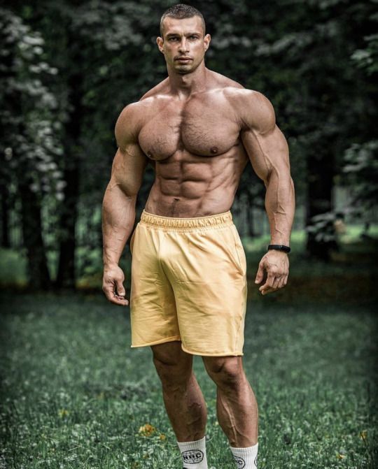 a shirtless man standing in the grass with his hands on his hips and looking at the camera