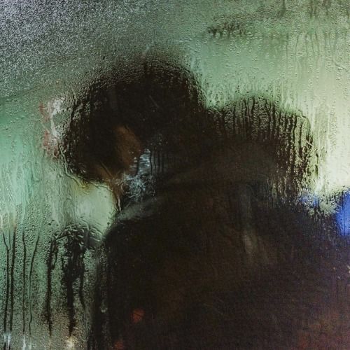 a blurry image of a person standing in front of a window with rain drops on the glass