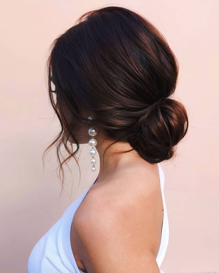 a woman with her hair in a low bun, wearing pearls on the side of her head