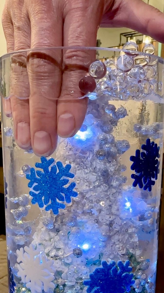 a person is holding their hand over a glass filled with water and snowflakes