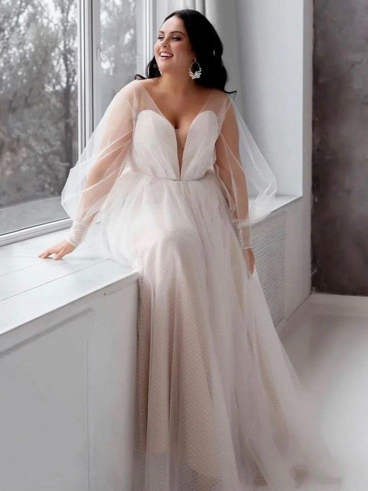 a woman standing next to a window wearing a wedding dress with long sleeves and a veil