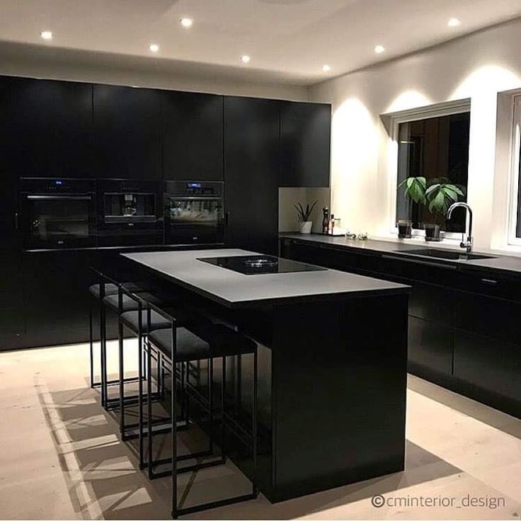 a modern kitchen with black cabinets and counter tops, lights on above the island area