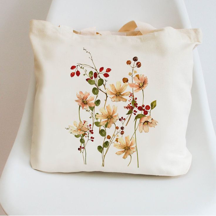 a white bag with flowers painted on it sitting on top of a chair next to a wall