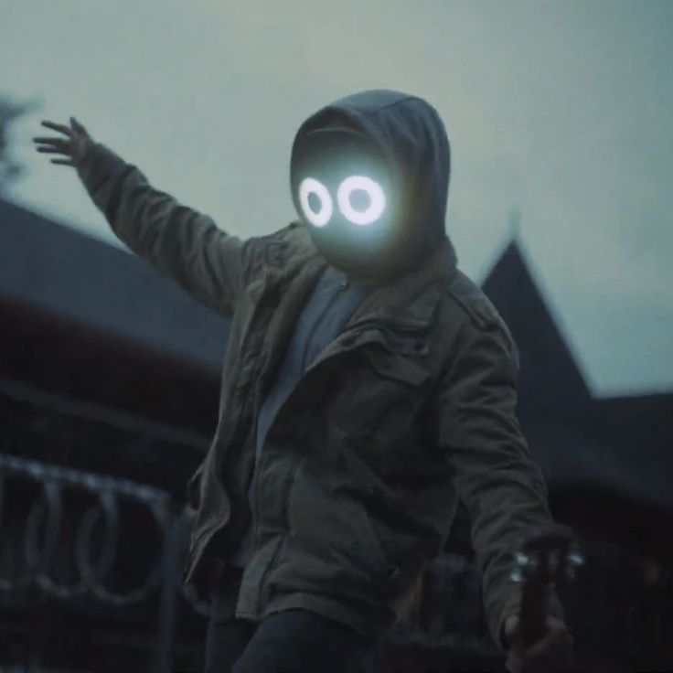 a man in a hooded jacket is holding out his arms with two glowing eyes on it