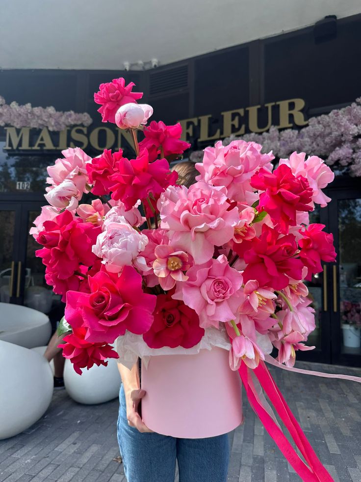 a woman is holding a pink bucket with flowers in it