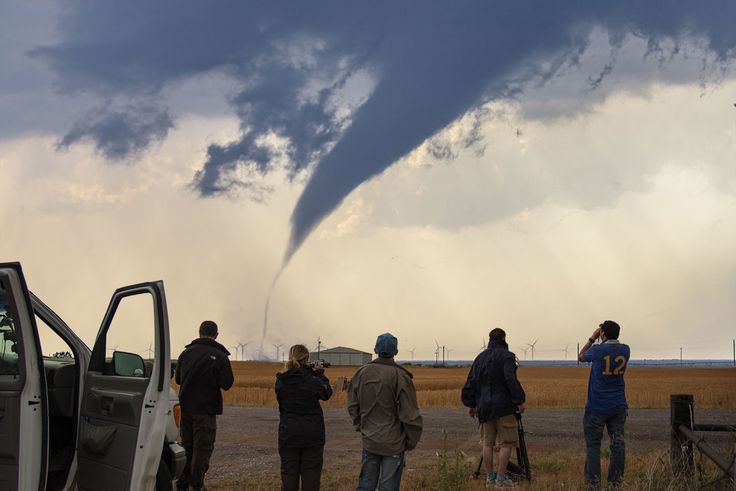 a group of people standing in front of a truck watching a large tornado roll through the sky