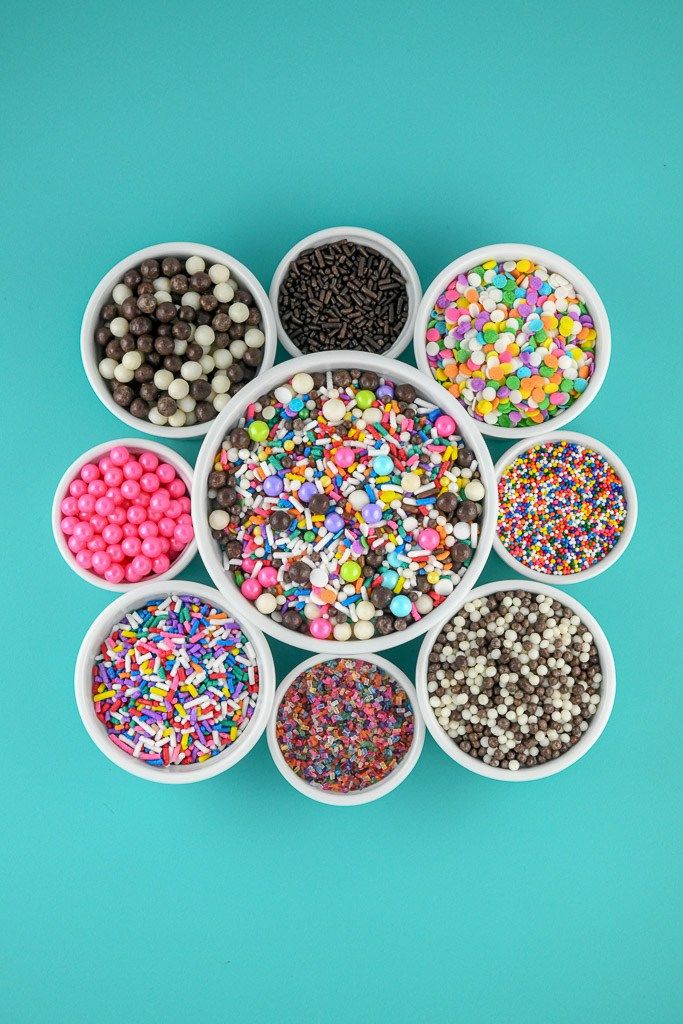 six cups filled with different colored sprinkles on top of a blue surface