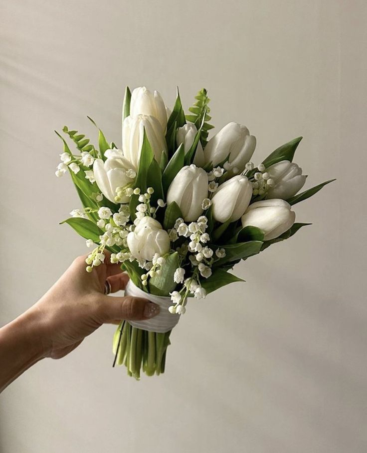 a bouquet of white tulips and lily of the valley in someone's hand