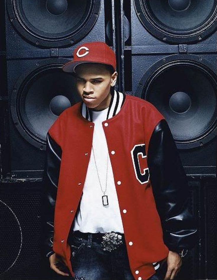 a man standing in front of speakers wearing a red and black baseball jacket with the letter c on it