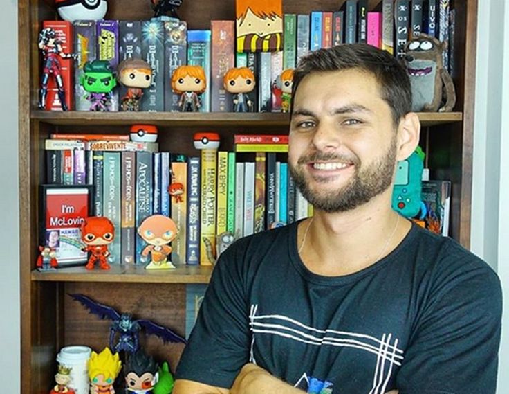 a man sitting in front of a bookshelf filled with lots of cartoon figures