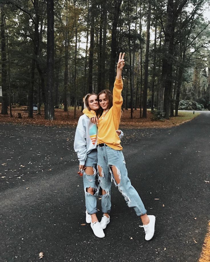 two young women standing on the side of a road taking a selfie with their arms in the air