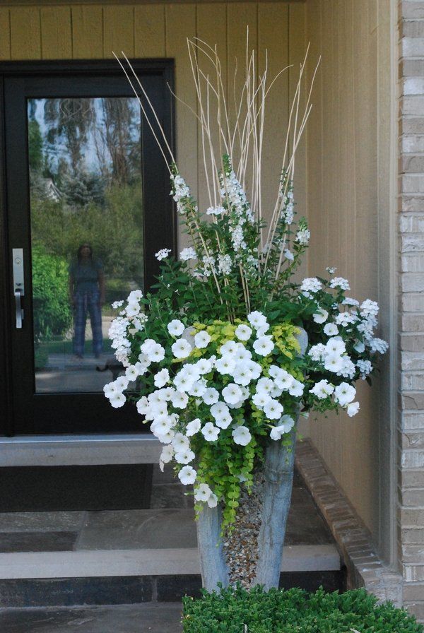 white flowers are in a vase on the steps outside an entranceway to a house