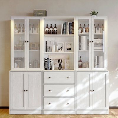 a white bookcase filled with lots of bottles and glasses next to a wall mounted clock