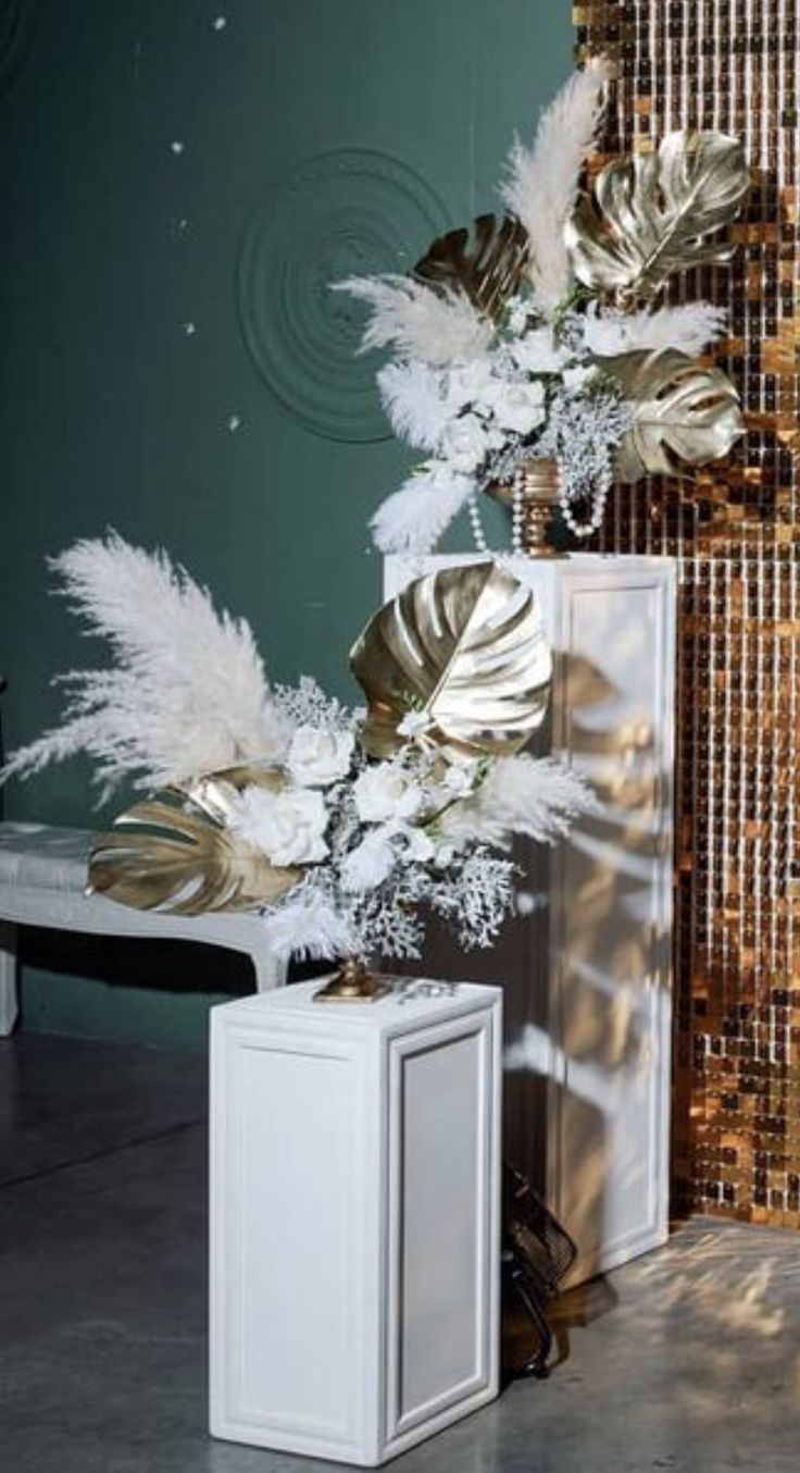 a white vase filled with lots of flowers next to a tall metal planter on top of a tiled floor