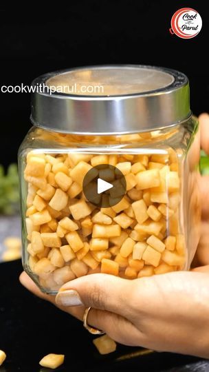 a person holding a glass jar filled with corn kernels on top of a table