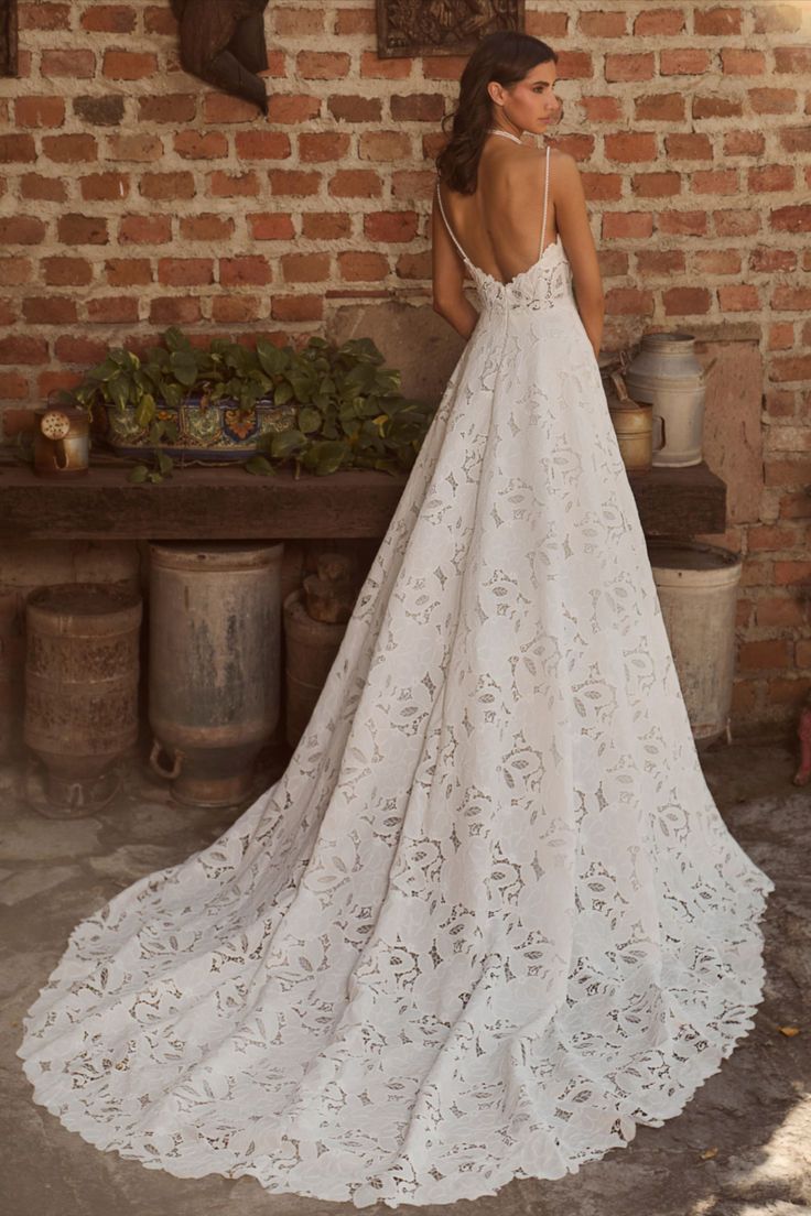 a woman standing in front of a brick wall wearing a wedding dress with an open back