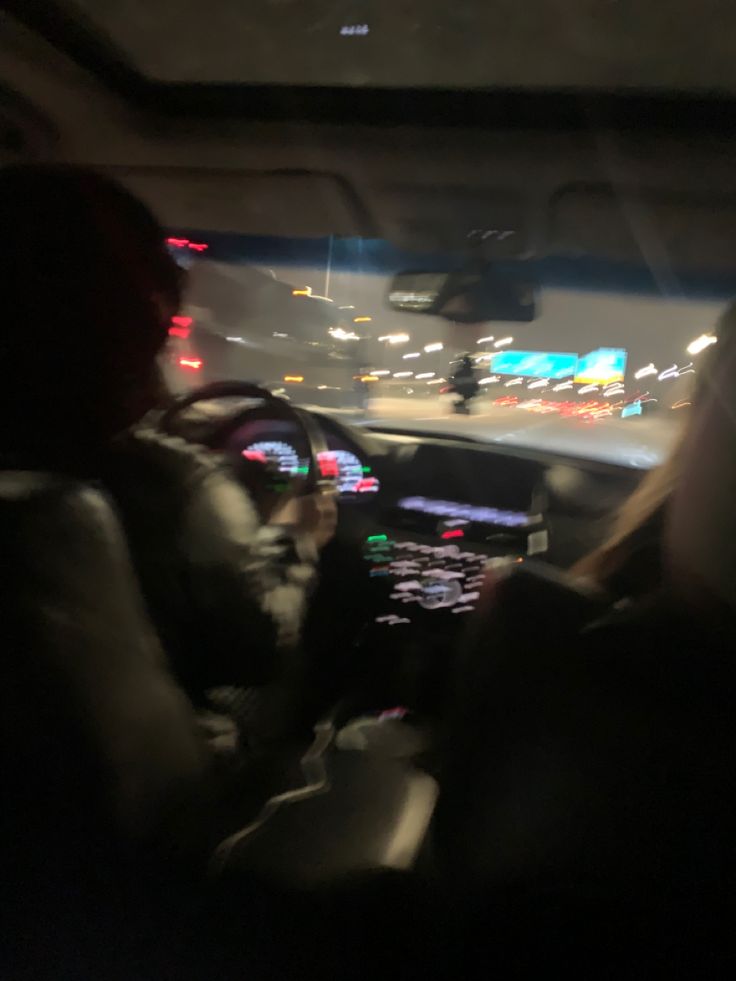 two people sitting in the passenger seat of a car at night with city lights behind them