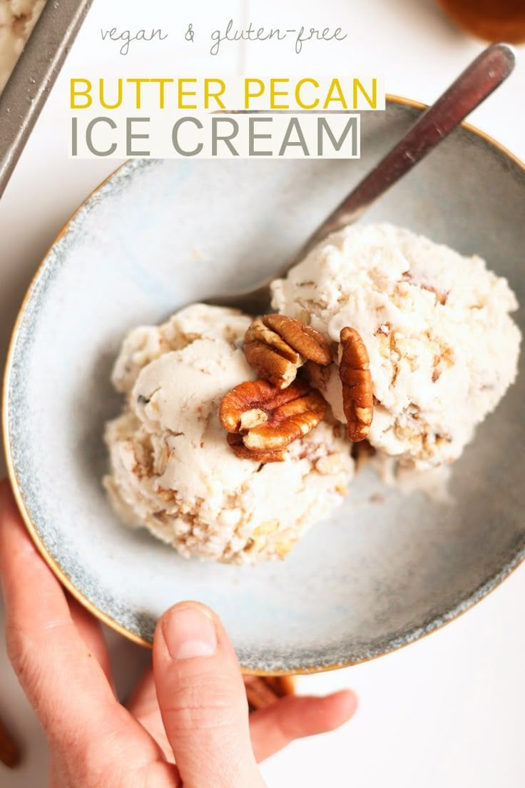 a person holding a plate with ice cream and pecans on it, next to a spoon