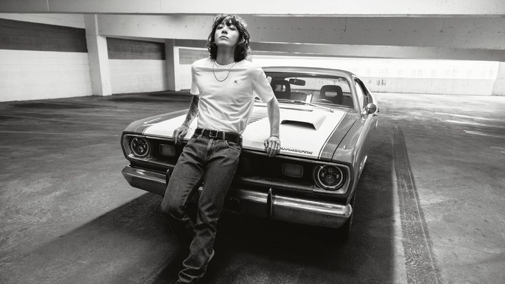 a woman sitting on the hood of a car in a parking garage with her head up