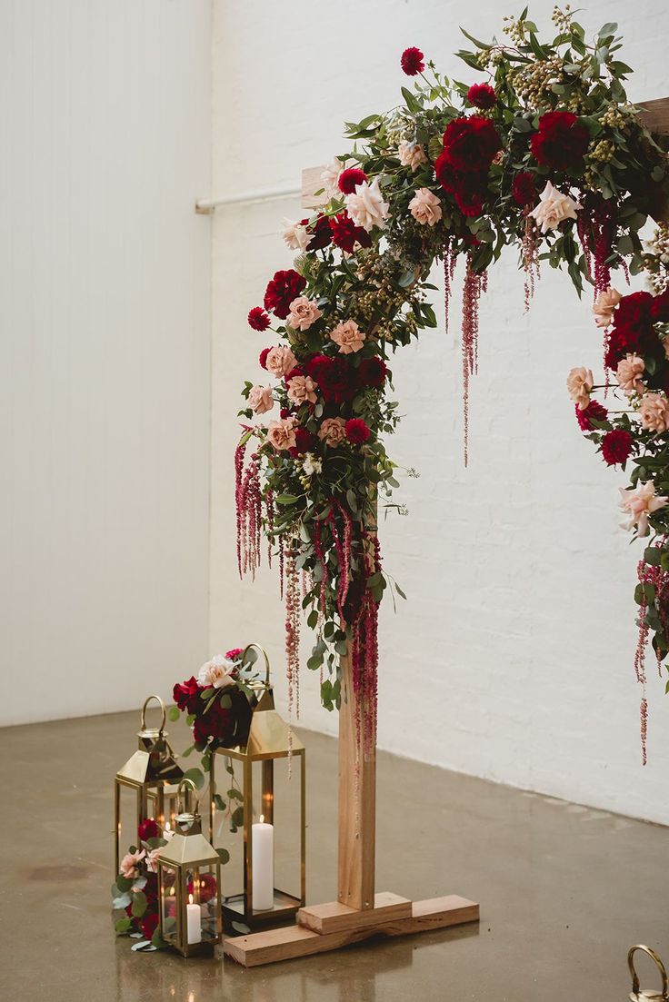 a wedding arch with flowers and candles on the floor in front of white brick wall