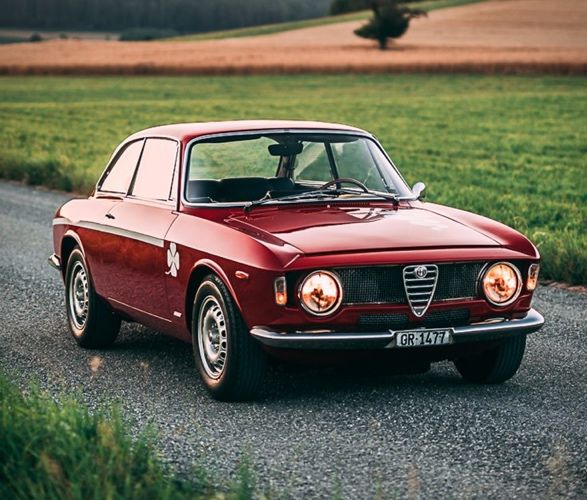 an old red car is parked on the side of the road in front of a field