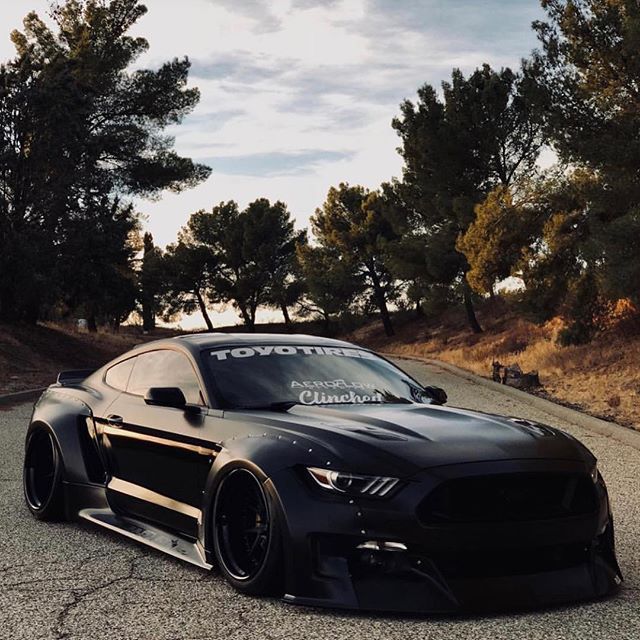 a black mustang parked on the side of a road with trees in the back ground