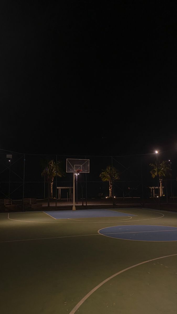 an empty basketball court at night with lights on