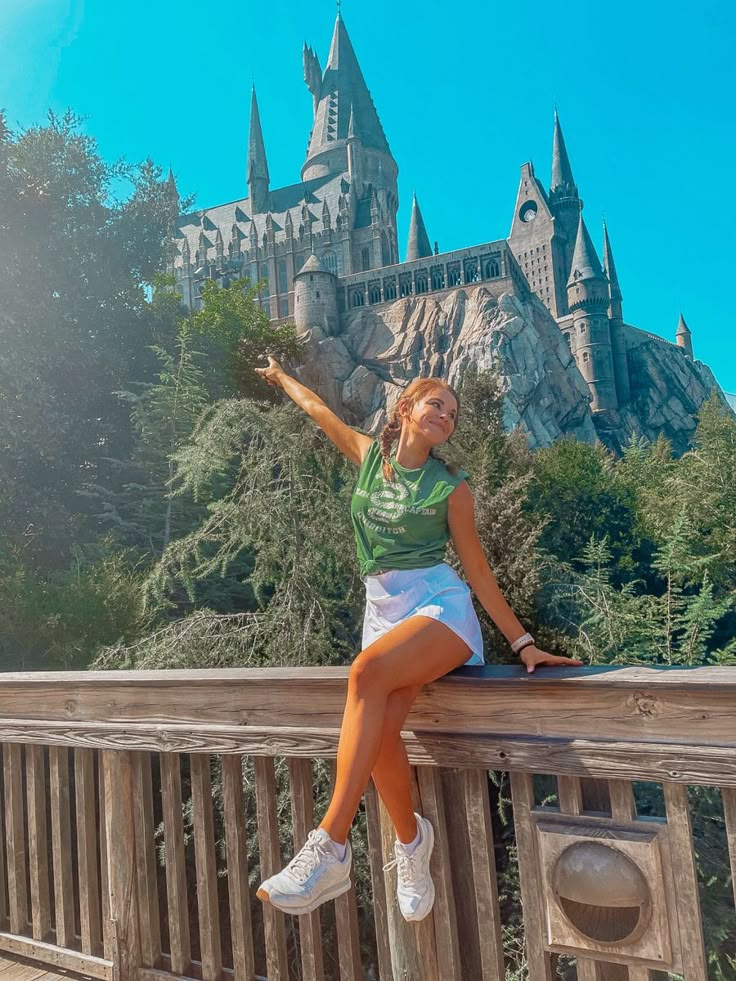 a woman sitting on top of a wooden fence next to a castle