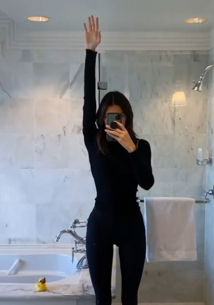 a woman taking a selfie in front of a bathroom mirror with her cell phone