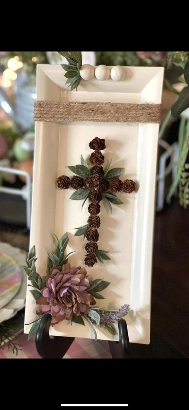 a cross made out of pine cones and flowers on a white plate with twine