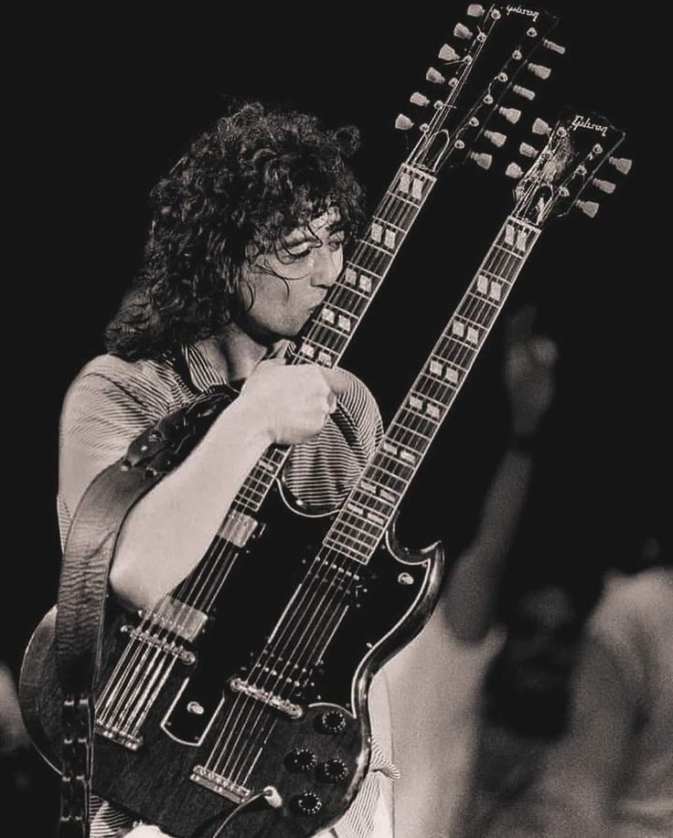 a black and white photo of a man playing an electric guitar with glasses on his face