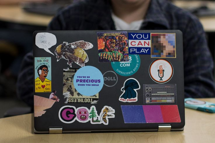 a person sitting at a table with a laptop covered in stickers and magnets