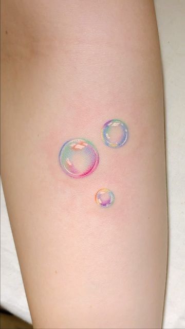 two soap bubbles on the back of a woman's leg, one is pink and blue