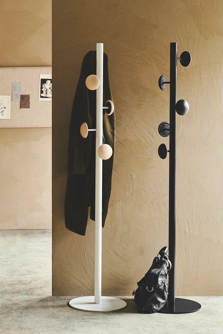 a coat rack with two coats hanging on it and a black bag next to it