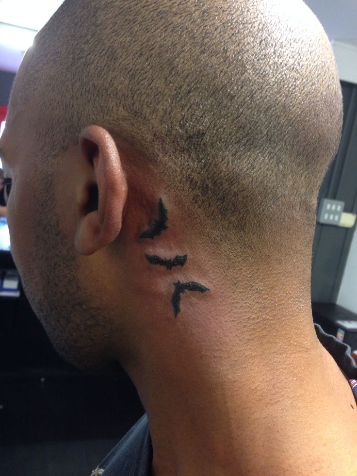 a man with a black bird tattoo on his left side of the neck behind his ear