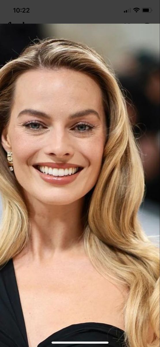 a woman with long blonde hair smiling and wearing a black dress on the red carpet