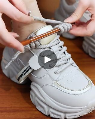 a person tying a shoelace on top of a white sneaker with grey laces