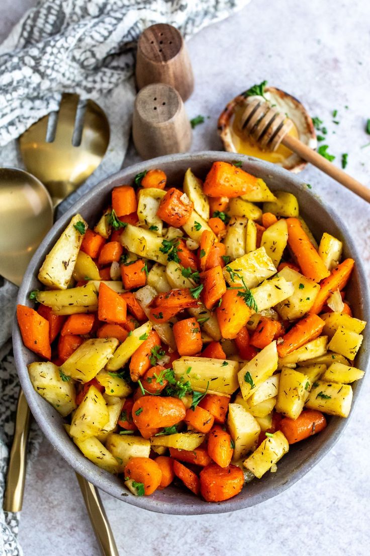 a bowl filled with carrots, potatoes and parsley next to two spoons