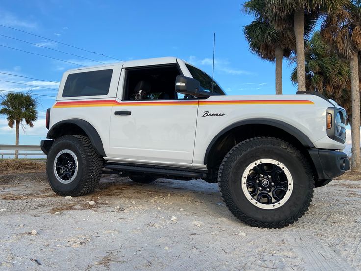 a white truck parked on top of a sandy beach next to the ocean and palm trees