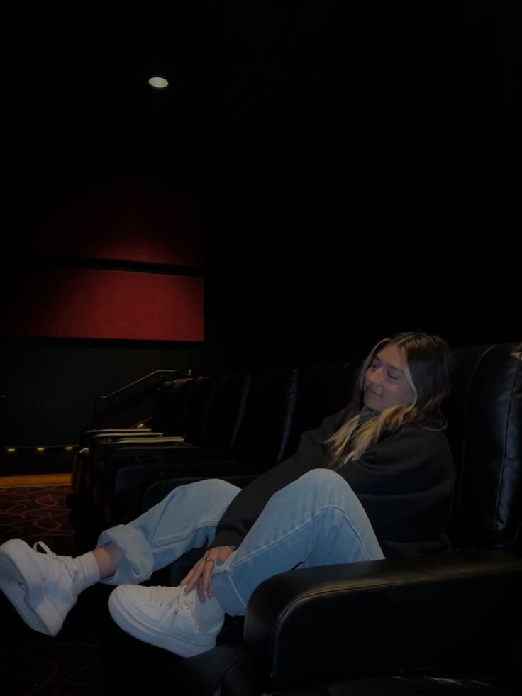 a woman sitting in a black chair with her feet up on the ground and looking at something