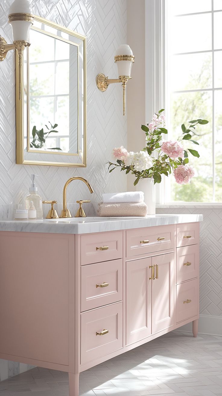 a bathroom with pink vanity and gold fixtures, flowers in vase on the sink counter