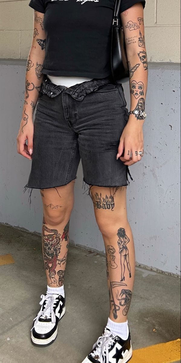 a woman with tattoos on her legs and arms standing in front of a white wall